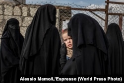 A Russian woman carries her child while waiting in line at a makeshift hospital in a camp in northern Syria housing the families of men who had fought for IS. (file photo)