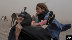 A frightened Afghan girl and woman receive aid on October 12 while enduring a fierce sandstorm after the earthquake in the Zenda Jan district of Herat Province.