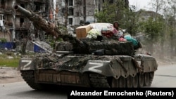 Russian or pro-Russian troops drive a tank along a street past a destroyed residential building in the town of Popasna in the Luhansk region on May 26, 2022.