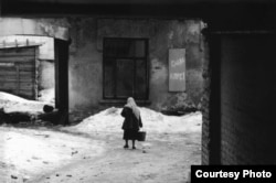 A woman in a Kyiv alleyway walks past a poster proclaiming, "Glory to the Communist Party!"