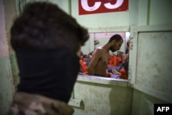 A member of the Syrian Democratic Forces (left) stands near IS inmates in a prison in northeast Syria. (file photo)