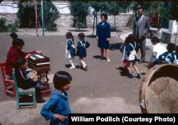 Young Afghan students dance on a school playground as a teacher and a student accompany on instruments.