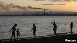 Residents walk along the shore of Lake Balkhash with a Soviet-era copper smelter in the background.