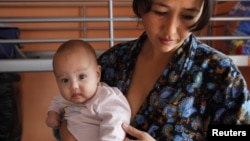 A single Tajik woman holds one of her twins in a shelter for women in crisis where she and other single women live outside Moscow.