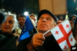 A demonstrator holds EU and Georgian national flags while attending an opposition protest against the results of the parliamentary elections, in Tbilisi on October 28.