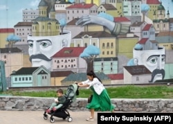 A woman pushes a stroller with her son in front of a mural in Kyiv.