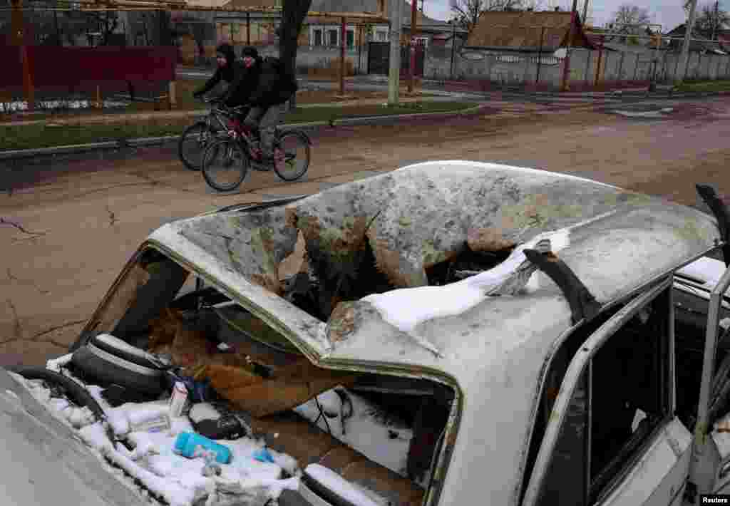 Residents ride bicycles near a car destroyed by Russian military strikes in the embattled Ukrainian frontline city of Pokrovsk. 