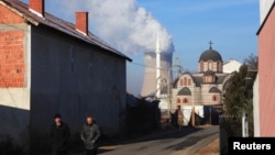 Men walk along the street in front of an Orthodox Church and a mosque as smoke billows out of the towers of a coal-fired power plant in Obilic, near Pristina, on December 5.