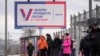 People wait at a bus stop next to a billboard promoting the upcoming presidential election in St. Petersburg in December.