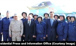 Russian President Vladimir Putin (front row, third left) and then-Syrian President Bashar al-Assad (front row, third right) pose for a photo with Russian pilots at the Hmeimim air base in Syria.