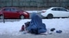 An Afghan woman holding her child begs on a snow-covered sidewalk in Kabul.