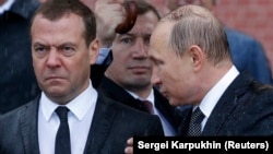 Russian President Vladimir Putin (right) speaks with Prime Minister Dmitry Medvedev in the rain during a ceremony at the Kremlin in Moscow in June 2017.