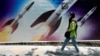 A woman walks past a banner showing missiles being launched in Tehran.