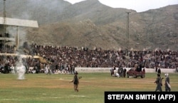 Taliban fighters and thousands of Kabul residents watch as surgeons cut off a thief's hand and the burning of hashish in the national stadium in 1998.