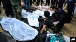 A man is comforted as he sits next to the covered body of a loved one who was killed in the explosions in the city of Kerman on January 3.