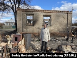 Lydia Prokopenko stands in front of the remains of her house, which was destroyed by a forest fire.