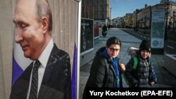 Russians walk near a large photograph of Russian President Vladimir Putin in the center of Moscow.