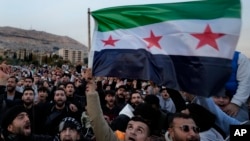 Syrian citizens wave the revolutionary flag and shout slogans as they celebrate in Damascus on December 9.