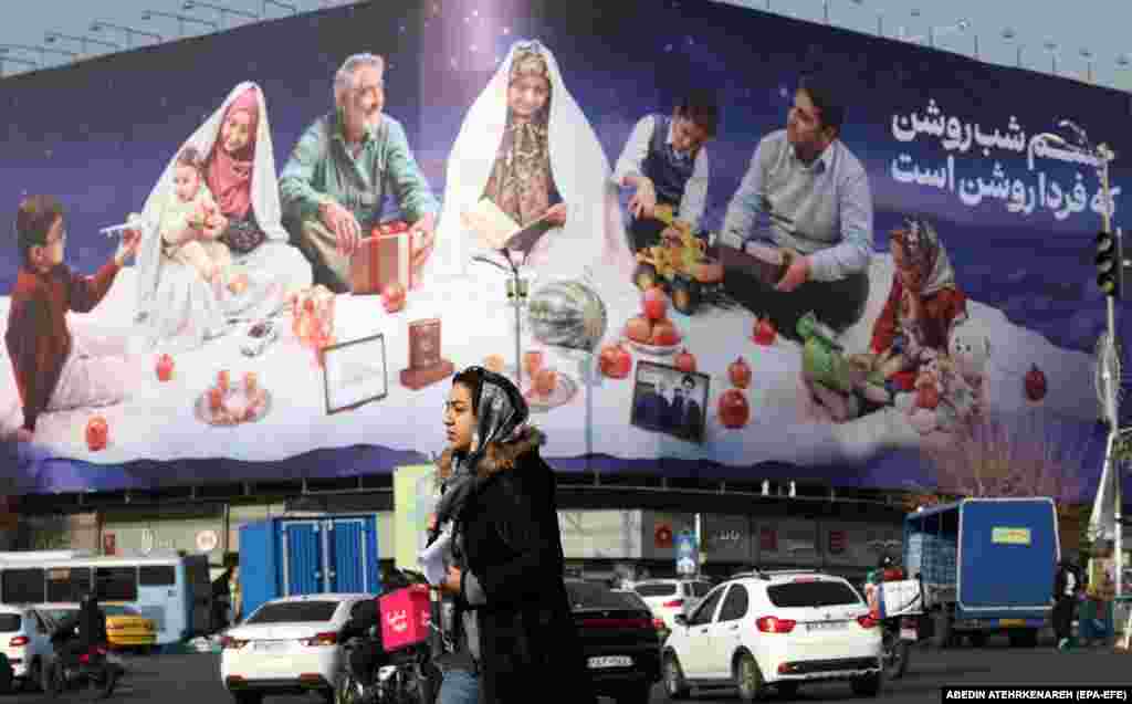 An Iranian woman walks past a billboard depicting an Iranian traditional family on Enghelab Square in Tehran.