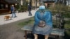 People walk their dogs past a sculpture wearing a protective mask in a park in central Kyiv.