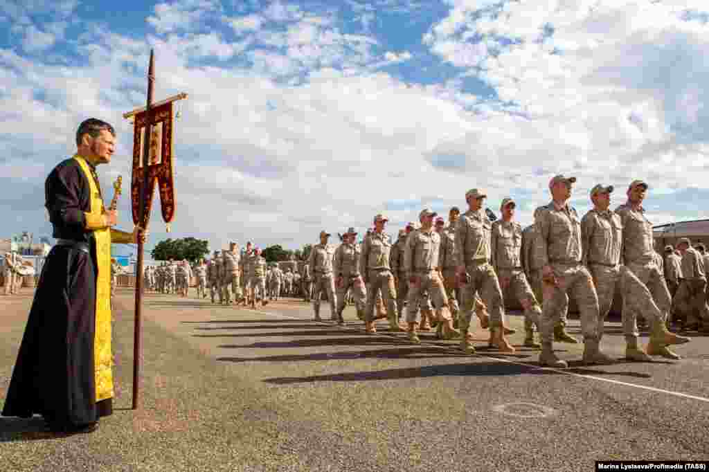 Russian troops march past an Orthodox priest at the Hmeimim base in April 2018. The soldiers are wearing sand-colored Russian uniforms issued to some servicemen based in Syria. Ben Dubow, a senior fellow at the Center for European Policy Analysis, told RFE/RL the current talks between Russia and HTS could result in &quot;a greatly reduced Russian presence,&quot; in the Syrian bases compared to the active combat phase during Assad&rsquo;s rule. &nbsp; &nbsp;