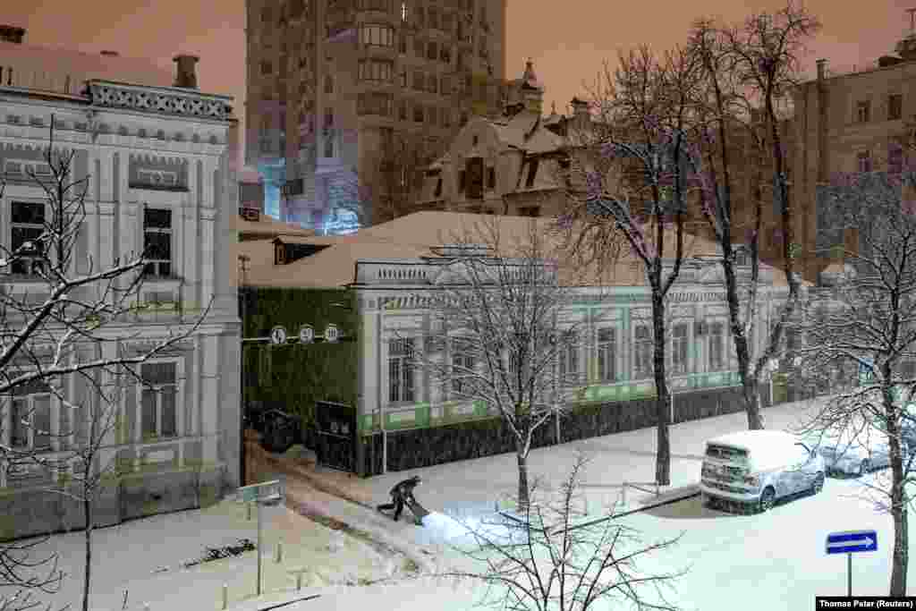 A man clears snow from a pavement on a snowy night in Kyiv. 